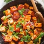 Savory tofu stir-fry with colorful vegetables in spicy sauce in a cast iron skillet, garnished with fresh herbs, highlighting healthy, delicious plant-based Asian cuisine.