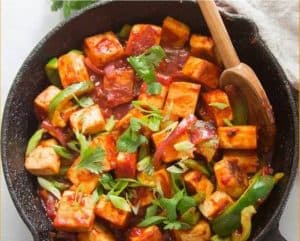 Savory tofu stir-fry with colorful vegetables in spicy sauce in a cast iron skillet, garnished with fresh herbs, highlighting healthy, delicious plant-based Asian cuisine.