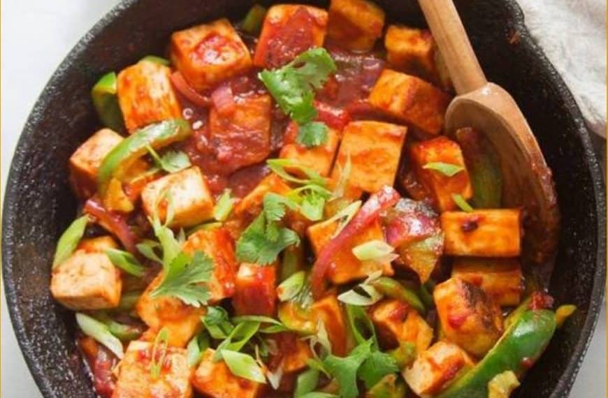 Savory tofu stir-fry with colorful vegetables in spicy sauce in a cast iron skillet, garnished with fresh herbs, highlighting healthy, delicious plant-based Asian cuisine.