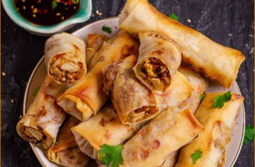 Crispy spring rolls filled with savory vegetables and meat, served with a side of sweet soy dipping sauce, on a dark textured surface garnished with cilantro.