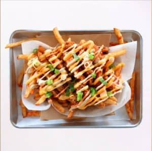 Crispy loaded fries topped with drizzled sauces, green onions, and crispy chicken pieces served in a stainless steel tray, perfect for sharing or enjoying as a flavorful snack.
