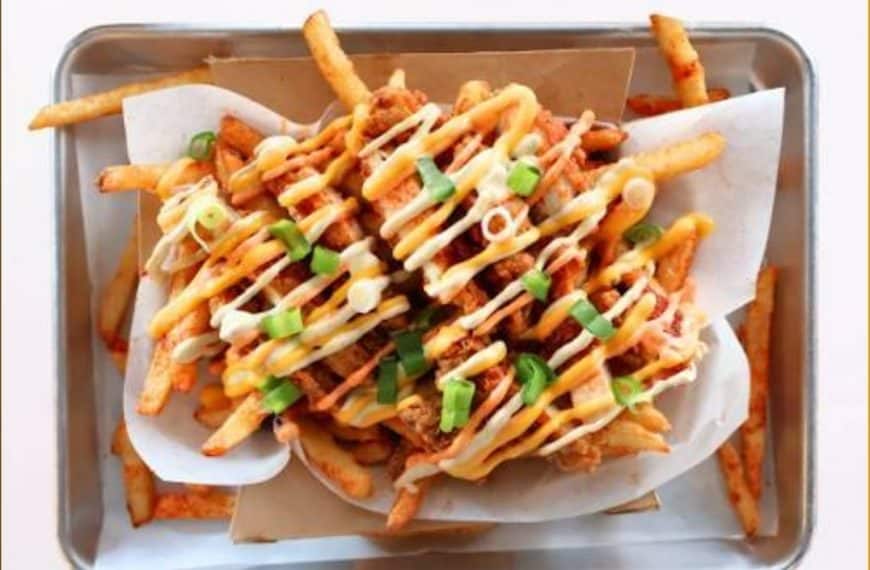 Crispy loaded fries topped with drizzled sauces, green onions, and crispy chicken pieces served in a stainless steel tray, perfect for sharing or enjoying as a flavorful snack.