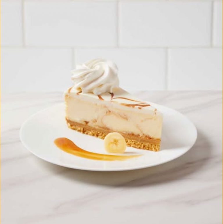 Creamy banana cheesecake with caramel drizzle and whipped cream on top on white plate.