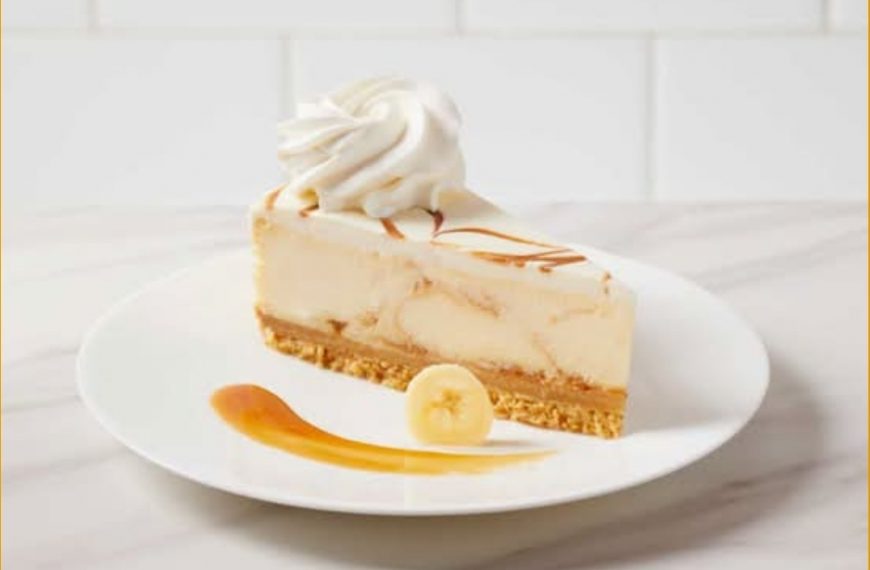 Creamy banana cheesecake with caramel drizzle and whipped cream on top on white plate.