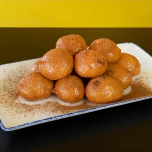 Golden fried dessert balls on a rectangular white plate, dusted with cinnamon powder, served for a delicious treat.