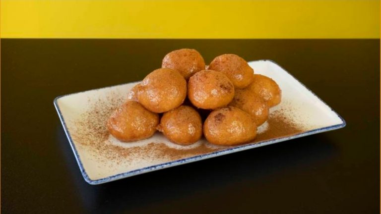 Golden fried dessert balls on a rectangular white plate, dusted with cinnamon powder, served for a delicious treat.