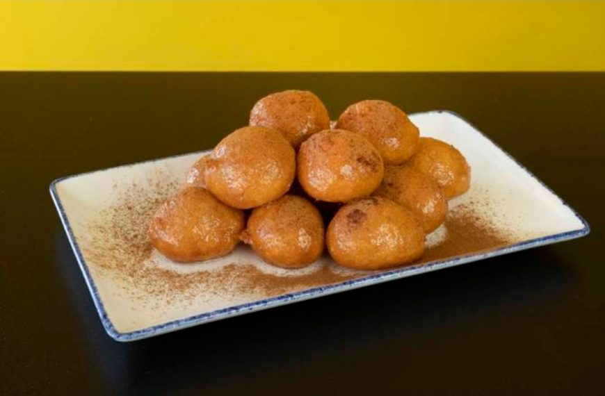Golden fried dessert balls on a rectangular white plate, dusted with cinnamon powder, served for a delicious treat.