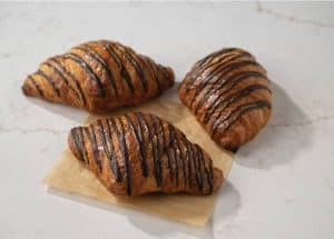 Buttery croissants drizzled with chocolate, fresh baked pastry, breakfast pastries, sweet croissants, homemade bakery treats.