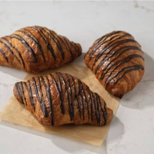 Buttery croissants drizzled with chocolate, fresh baked pastry, breakfast pastries, sweet croissants, homemade bakery treats.