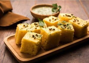 Fluffy Indian cornbread (Makai ka Saag) garnished with fresh herbs and black cumin seeds, served on a wooden platter with green chutney on the side, ideal for traditional Indian cuisine.