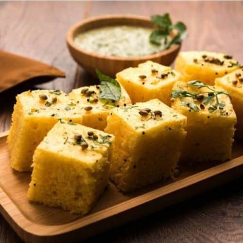 Fluffy Indian cornbread (Makai ka Saag) garnished with fresh herbs and black cumin seeds, served on a wooden platter with green chutney on the side, ideal for traditional Indian cuisine.