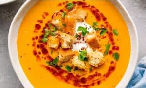 Creamy butternut squash soup with croutons, fresh herbs, and a swirl of chili oil, served in a white bowl for a comforting and flavorful vegetarian meal.