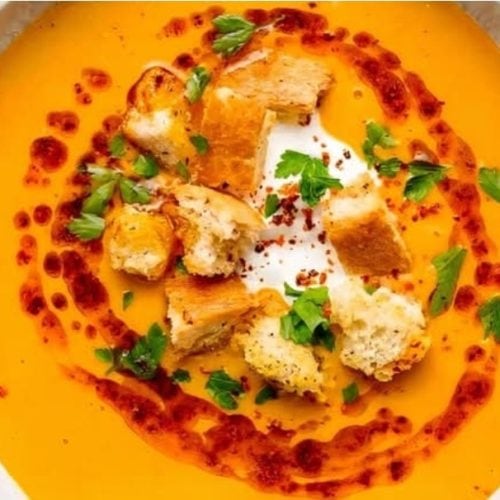 Creamy butternut squash soup with croutons, fresh herbs, and a swirl of chili oil, served in a white bowl for a comforting and flavorful vegetarian meal.