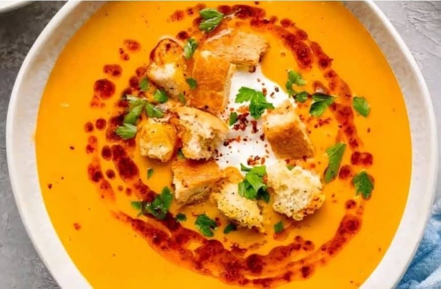 Creamy butternut squash soup with croutons, fresh herbs, and a swirl of chili oil, served in a white bowl for a comforting and flavorful vegetarian meal.