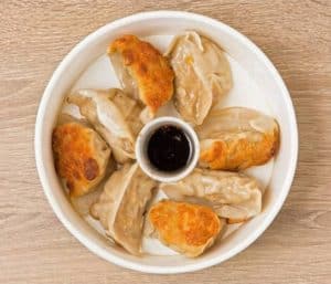 Succulent steamed dumplings with crispy fried tops served on a white plate with soy sauce dip for dipping and flavor enhancement.
