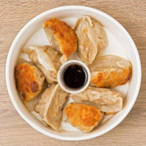 Succulent steamed dumplings with crispy fried tops served on a white plate with soy sauce dip for dipping and flavor enhancement.
