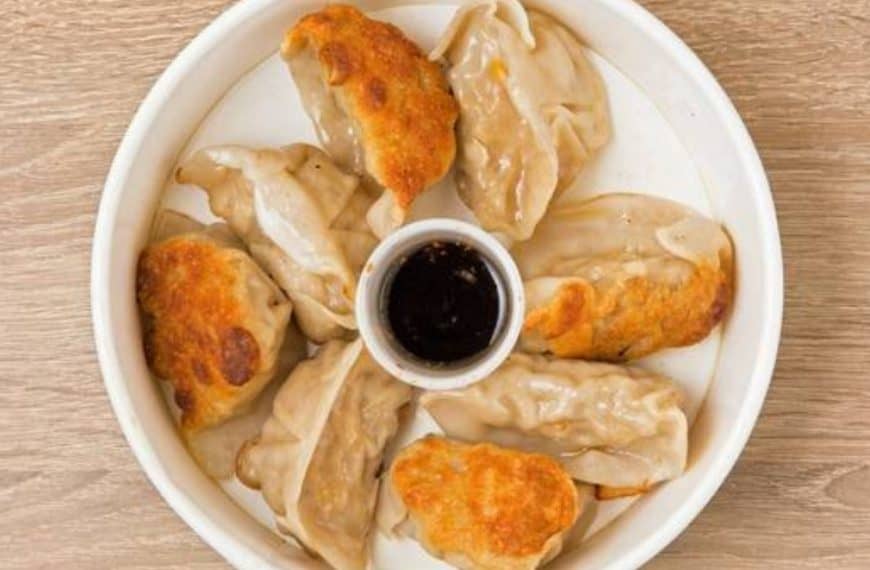 Succulent steamed dumplings with crispy fried tops served on a white plate with soy sauce dip for dipping and flavor enhancement.
