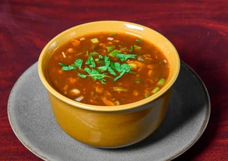 Hearty bowl of vegetable beef soup garnished with fresh cilantro, served in a yellow bowl on a dark wooden table, perfect for a comforting homemade meal.