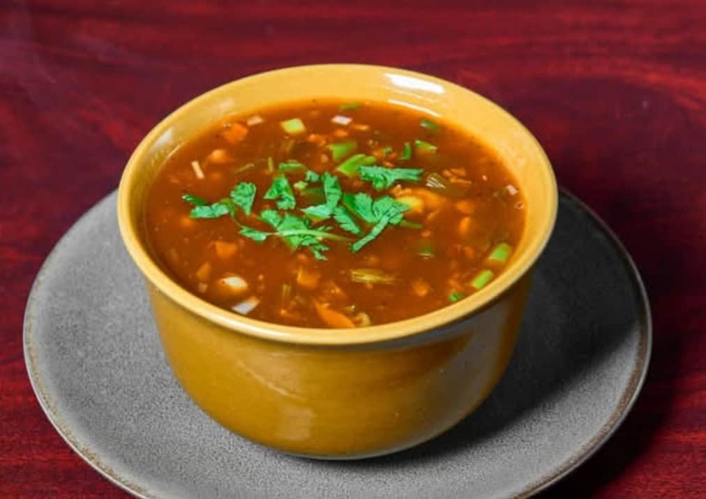 Hearty bowl of vegetable beef soup garnished with fresh cilantro, served in a yellow bowl on a dark wooden table, perfect for a comforting homemade meal.