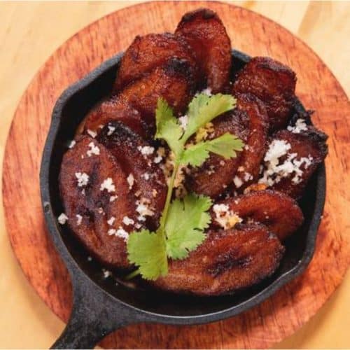 Crispy fried chicken wings garnished with cilantro and sprinkled with coarse salt served in a cast iron skillet on a wooden tray.