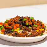 Savory beef stew served over rice with colorful vegetables, cilantro garnish, and rich tomato sauce, perfect for hearty comfort food meals.